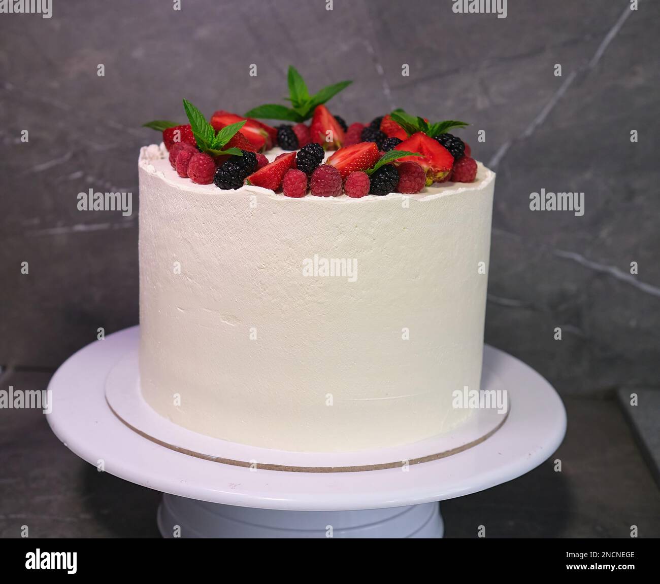 Köstlicher hausgemachter weißer Cremetorte mit Beeren und grünen Minzblättern Stockfoto