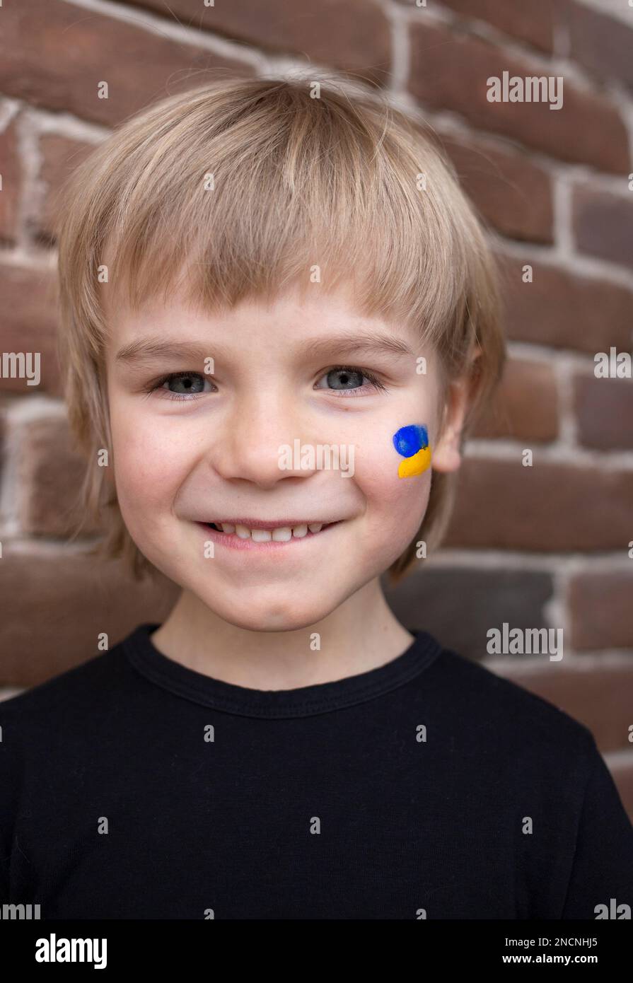Porträt des Gesichts eines glücklichen, lächelnden Jungen, eine gelb-blaue Flagge der Ukraine wird auf seine Wange gezeichnet. Patriotische Erziehung. Die Kinder der Ukraine wollen sport Stockfoto