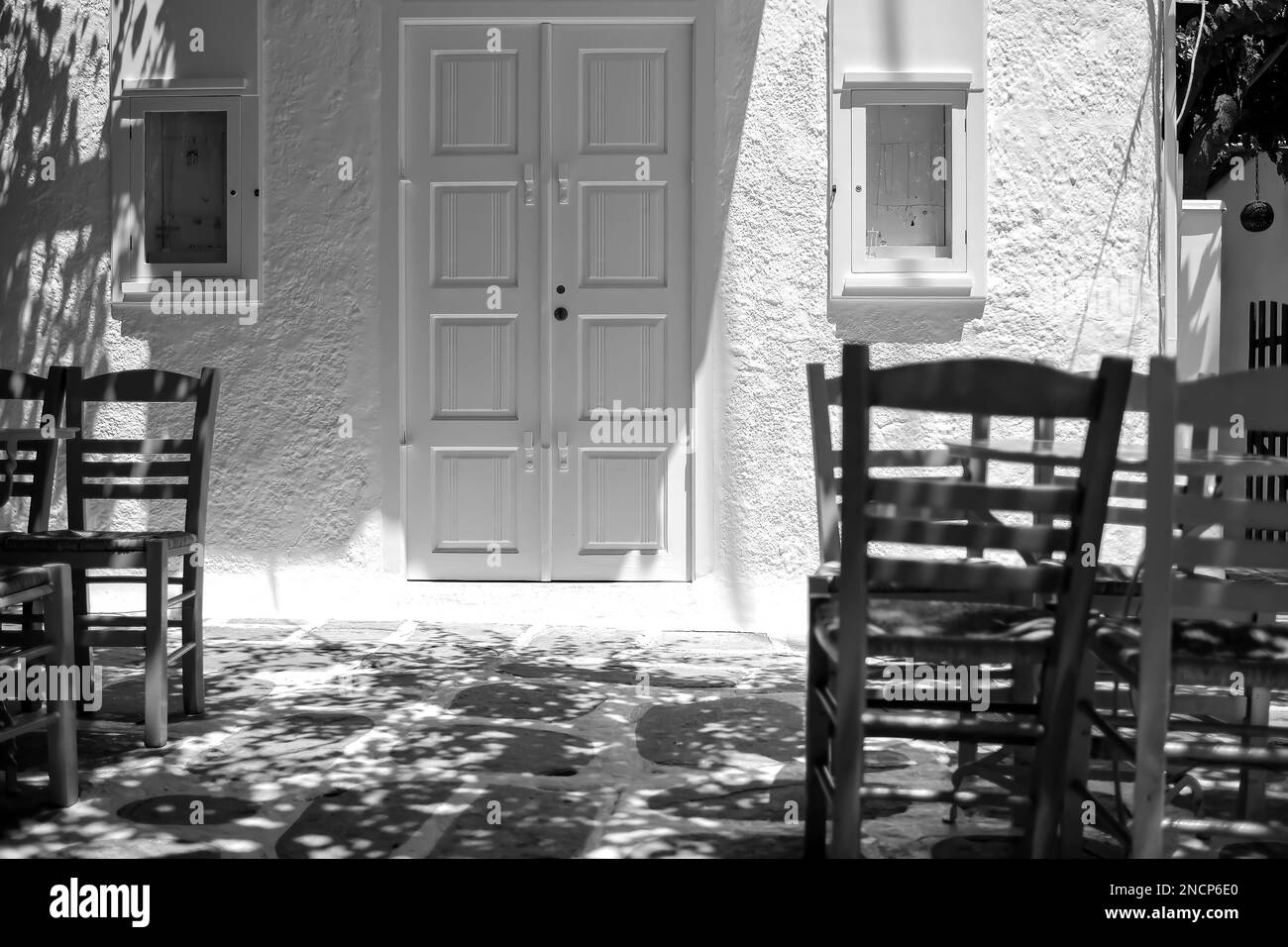 Blick auf farbenfrohe Stühle, Tische und ein weiß getünchtes Geschäft im Hintergrund in iOS Griechenland in Schwarz und Weiß Stockfoto