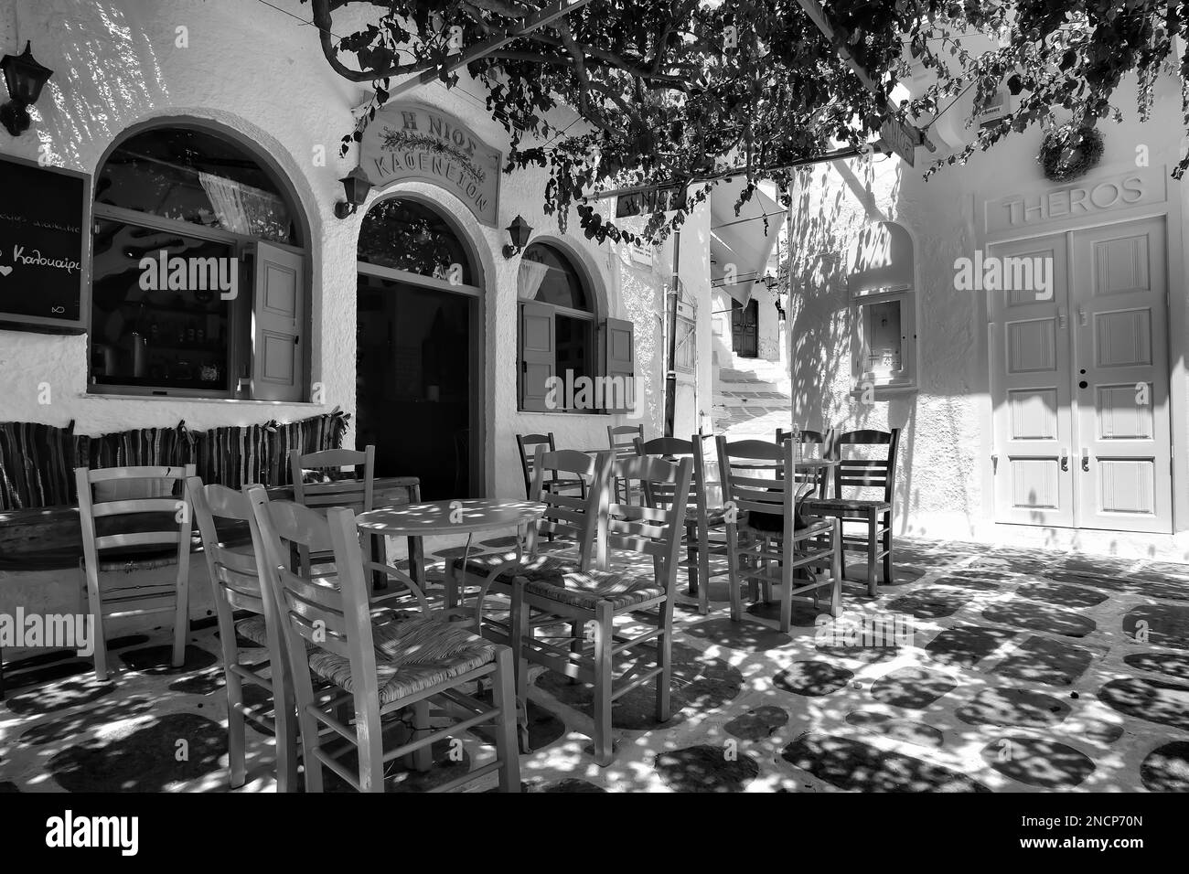 IOS, Griechenland - 2. Juni 2021 : Blick auf ein Bar-Restaurant mit malerischer Terrasse im Freien und farbenfrohen Stühlen in den iOS kykladen Griechenlands in Schwarz und Weiß Stockfoto