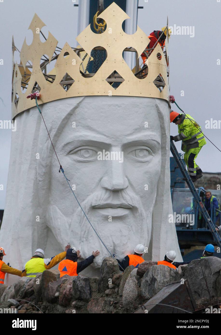 Workers raise the crowned head of a statue of Jesus before placing it