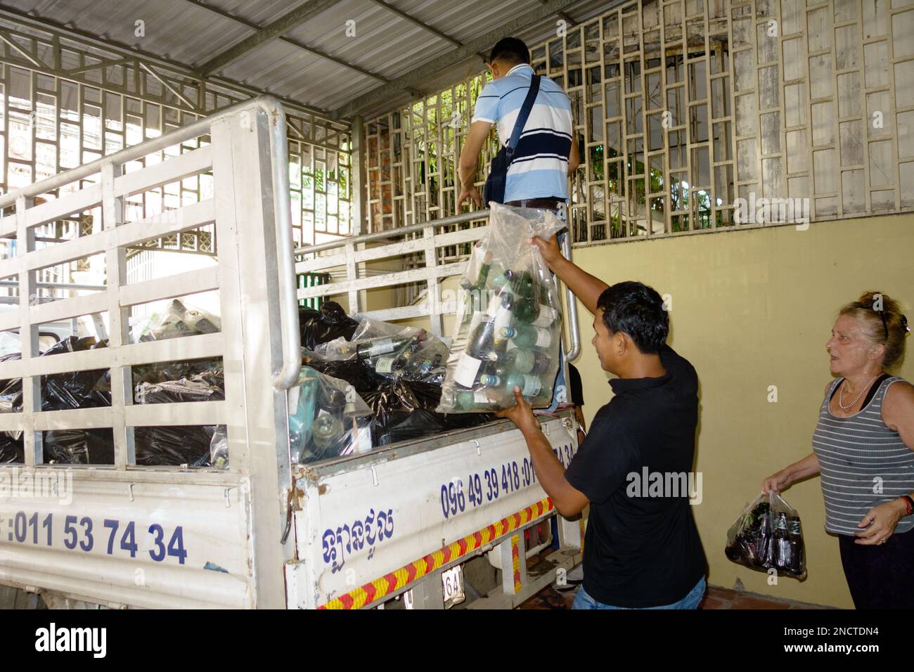 Freiwillige in Phnom Penh, Kambodscha sammeln Recycling und transportieren es zur Kokosnussschule, die aus Abfallmaterialien gebaut wird. Stockfoto