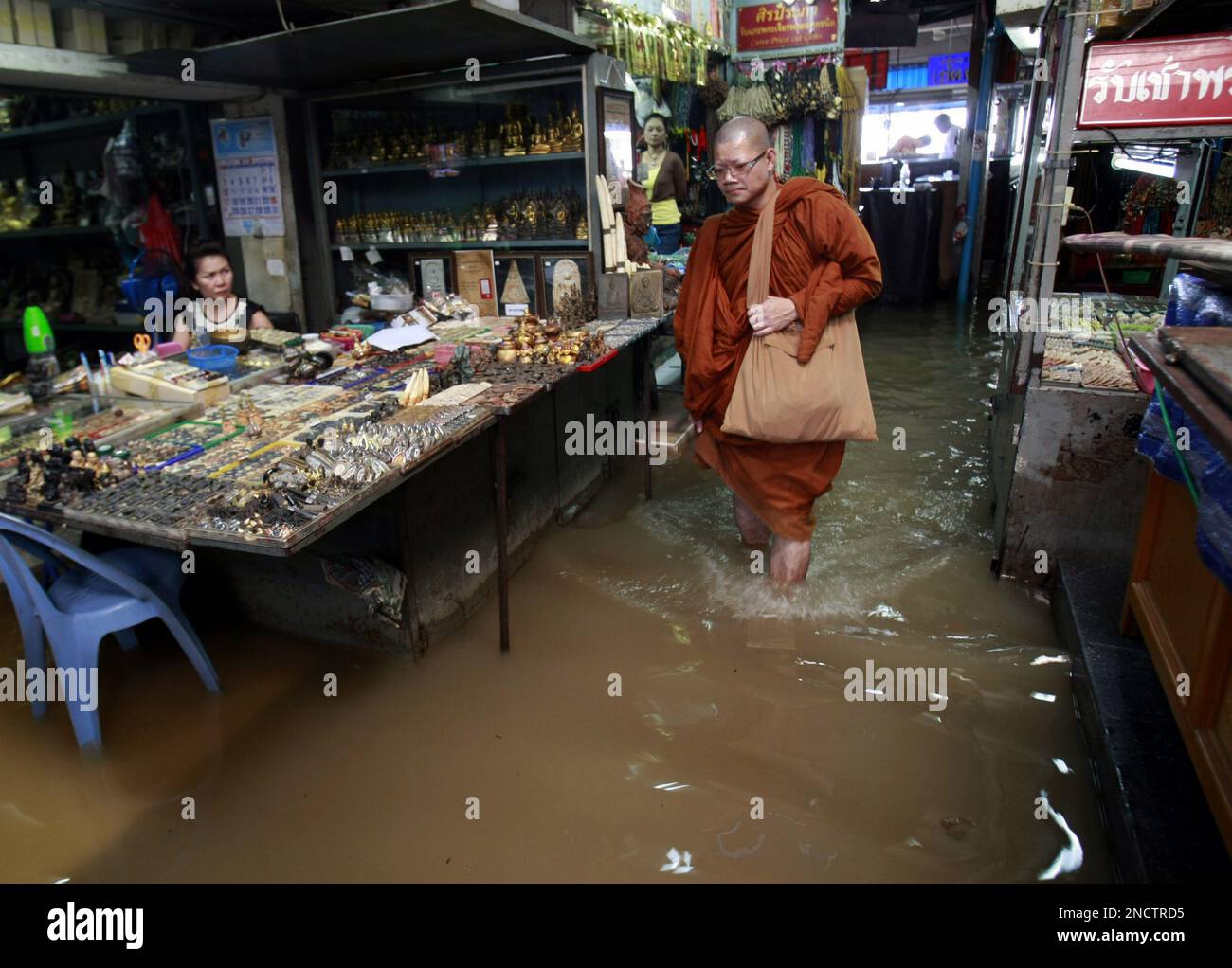 A Buddhist monk wades through a flooded small business area near the Chao Phraya river Monday, Oct. 25, 2010 in Bangkok, Thailand. High tide combined with increasing water level after large volume of water from the country's northern part flew in to the Chao Phraya river have made the area near the river in the Thai capital temporarily inundated. (AP Photo/Apichart Weerawong) Stockfoto