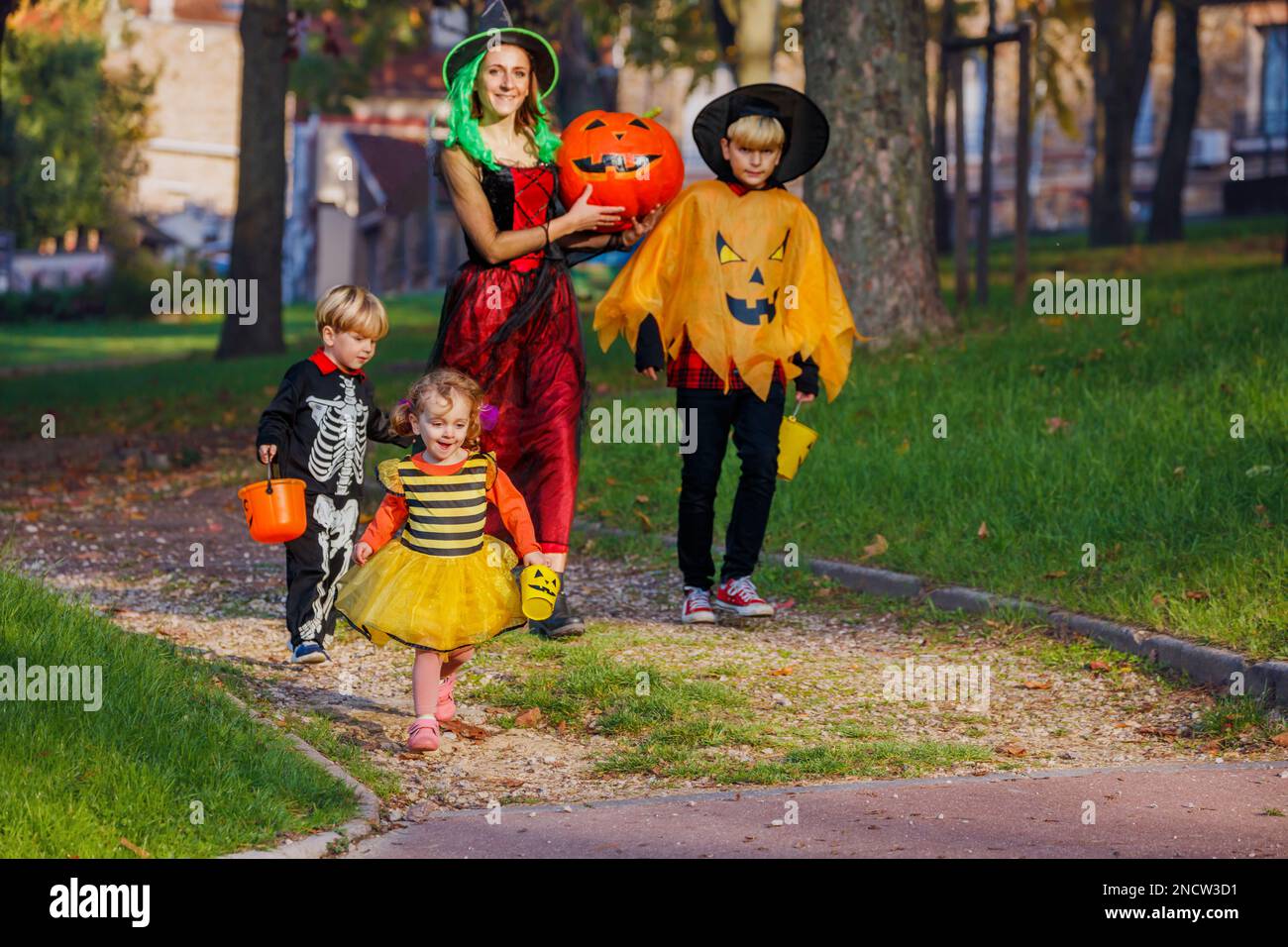 Frauen gehen mit Kindern in Halloween-Kostümen und halten Süßigkeiten-Eimer Stockfoto