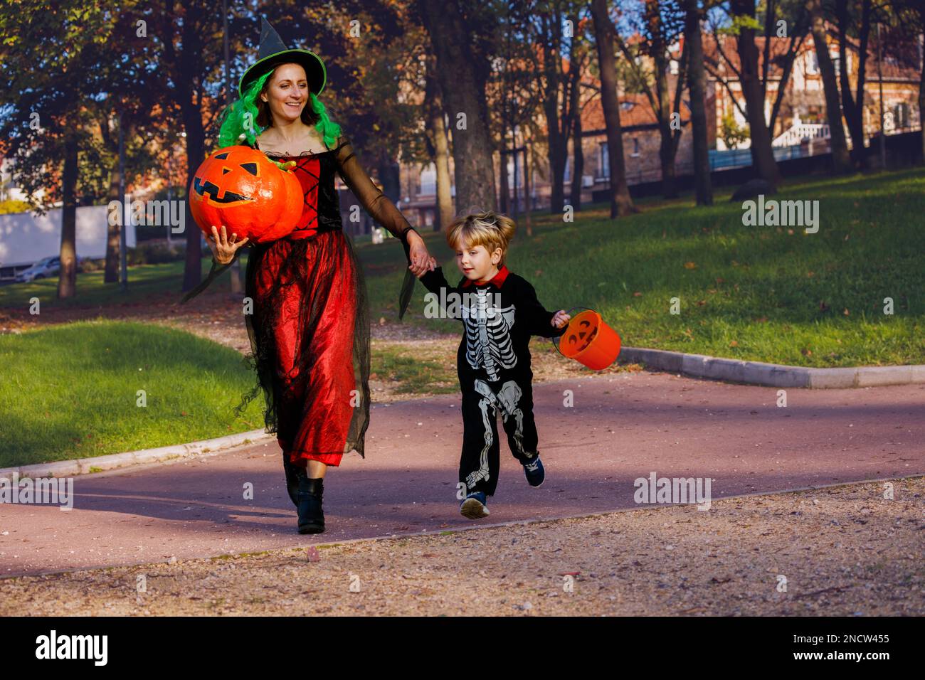 Mutter und Junge Rennen in Skelettkostümen, Hexe hält Eimer Stockfoto