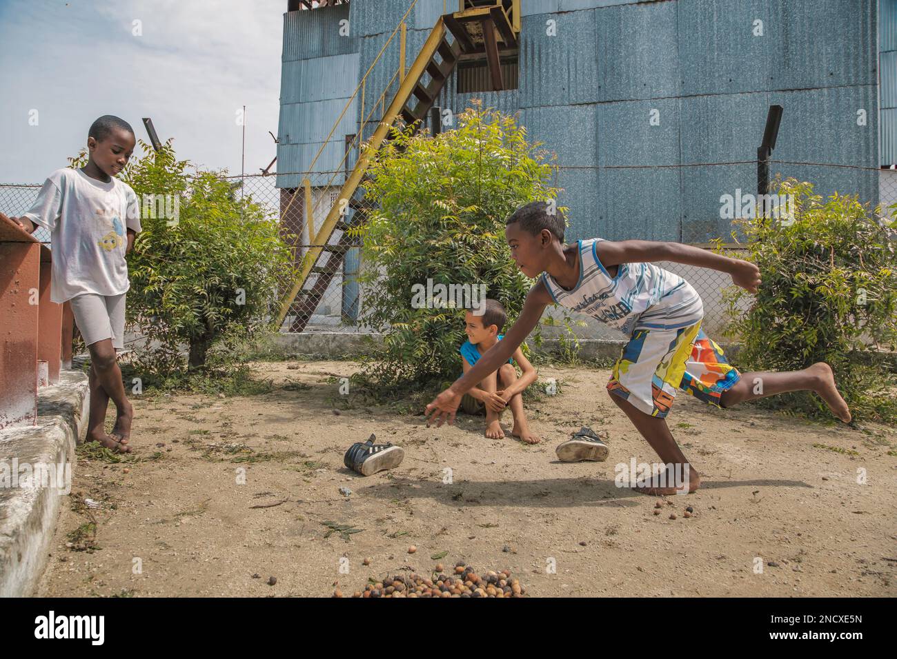 Augusto César Sandino, Artemisa, Kuba. 12. Juli 2019. Zwei schwarze Jungs und ein weißer Junge, die barfuß im Dreck mit trockenen Samen Murmeln spielen, in Kuba. Stockfoto