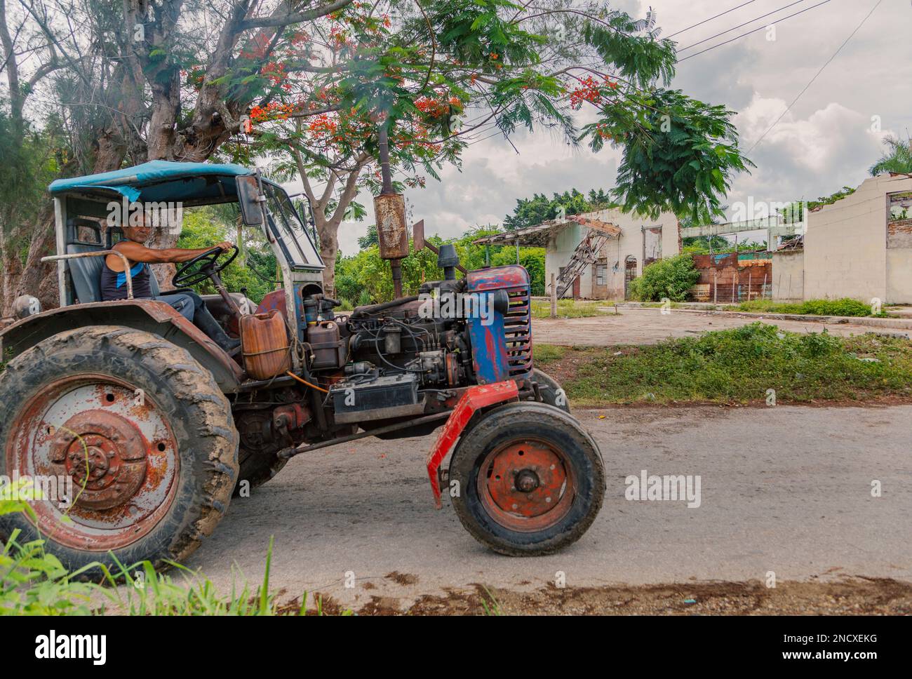 Augusto César Sandino, Artemisa, Kuba. 11. Juli 2019. Ein Bauer, der einen Traktor auf einer Straße mit einem zerstörten Gebäude im Hintergrund in einer Landstadt fährt. Stockfoto