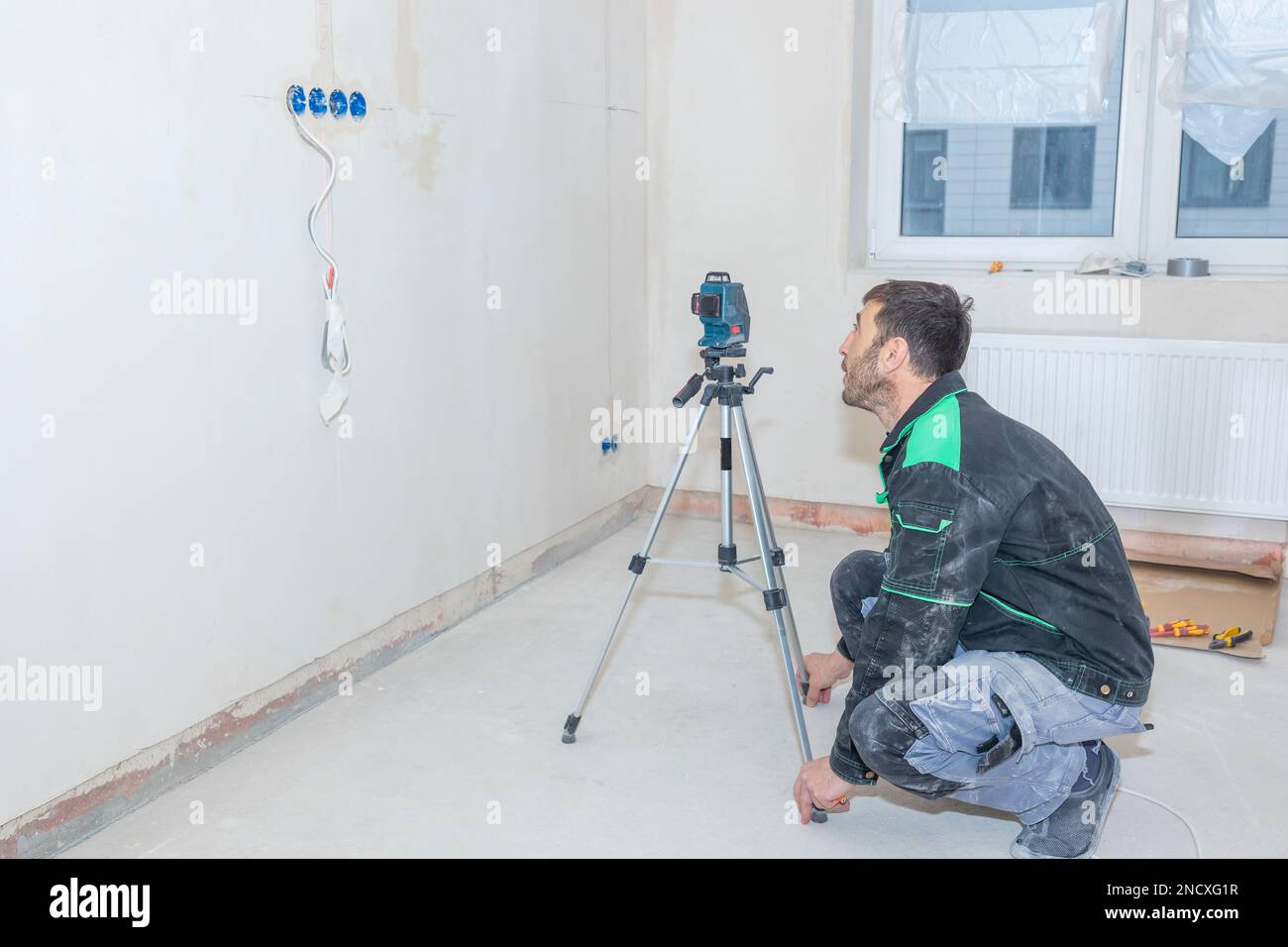Der Mann repariert in einer neuen Wohnung. Der Baumeister nivelliert die Wände mit einer Laserwaage. Hochwertiges Foto Stockfoto