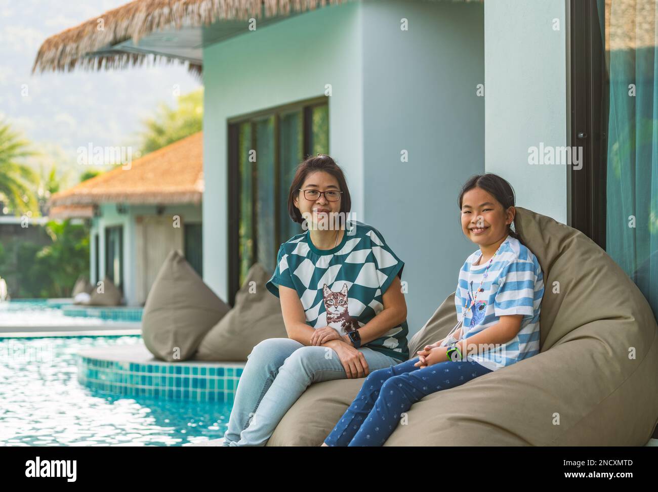 Porträt asiatische Mutter und Tochter sitzen auf einem Sitzsack am Pool eines Resorts, eine Frau mittleren Alters und ein Mädchen mittleren Alters im Alter von 8 oder 9 Jahren. Stockfoto