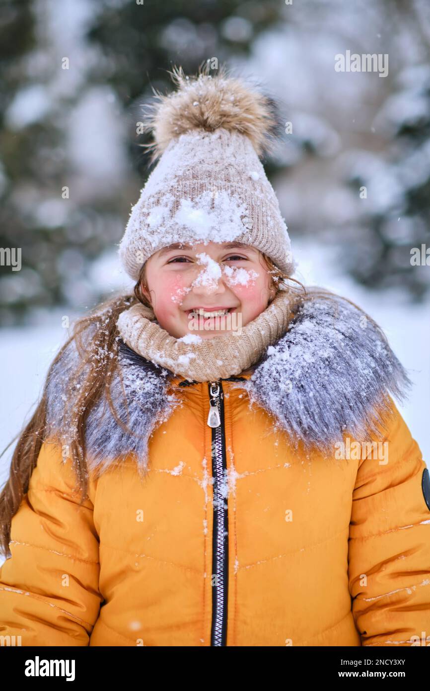 Nahaufnahme eines glücklichen Mädchens in einer pelzigen Kapuze, lustiges kleines Mädchen, das während des Schneefalls im wunderschönen Winterpark Spaß hat Stockfoto