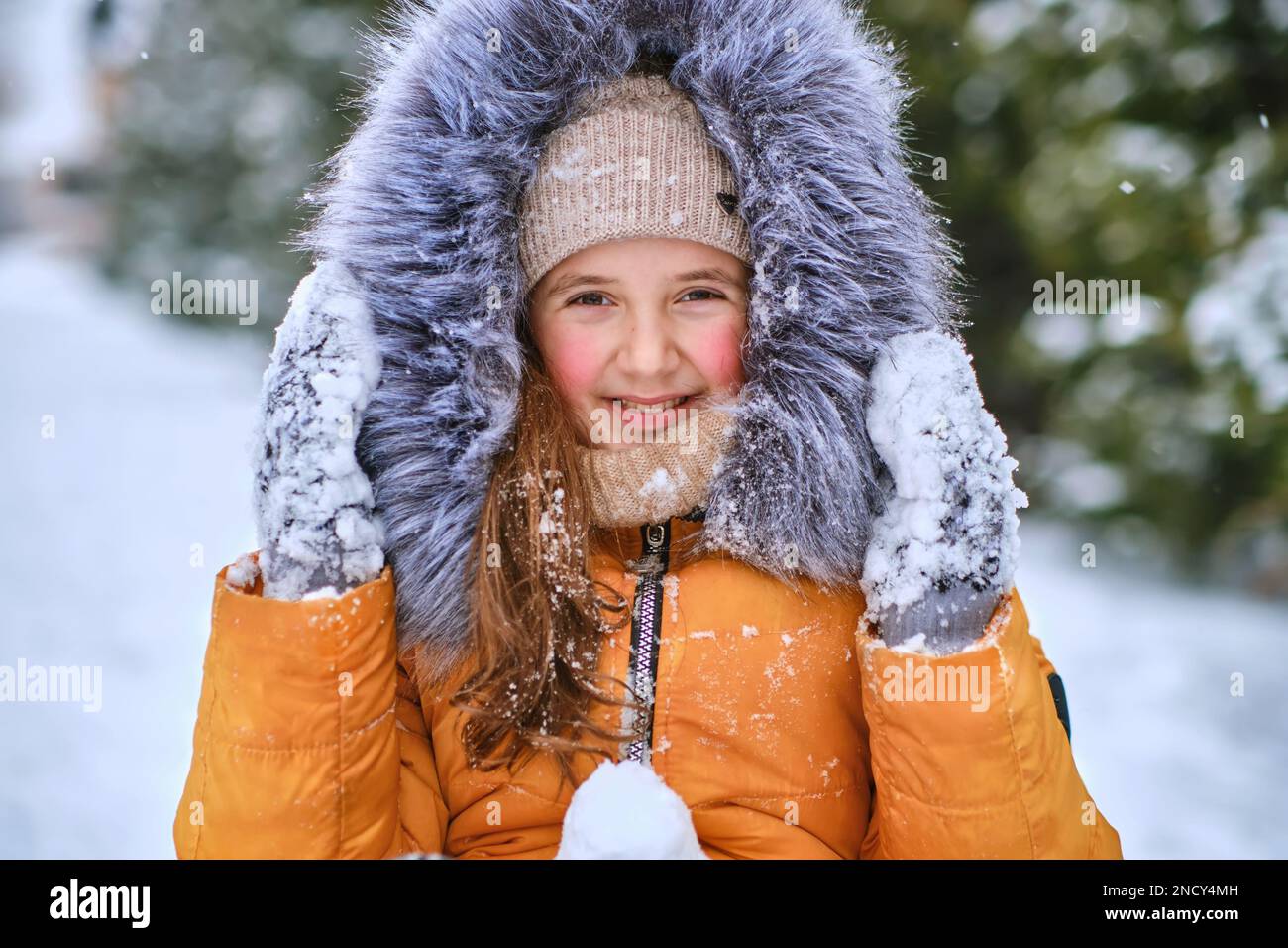 Nahaufnahme eines glücklichen Mädchens in einer pelzigen Kapuze, lustiges kleines Mädchen, das während des Schneefalls im wunderschönen Winterpark Spaß hat Stockfoto