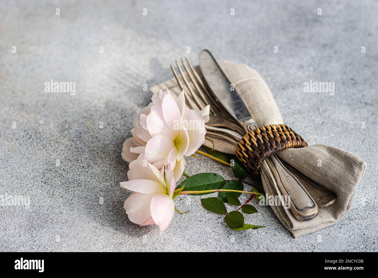 Nahaufnahme eines Bestecksets in einem Serviettenring mit weißen Rosen auf einem Tisch Stockfoto