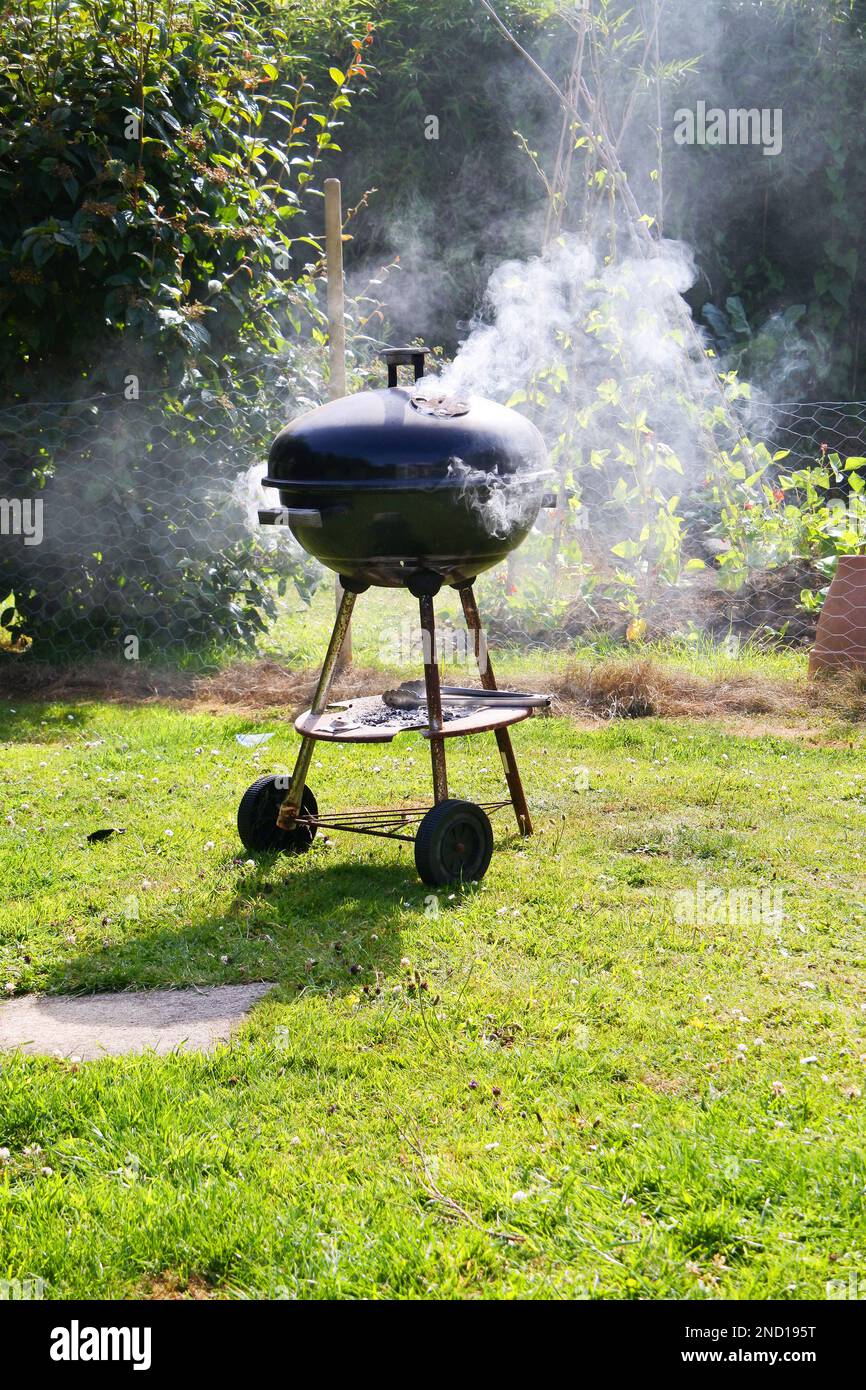 Rauchen Sie ein Barbecue mit heißem Wasserkocher in einer Gartenumgebung - John Gollop Stockfoto