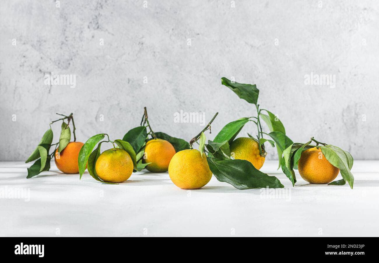 Orange Zitrusfrüchte Tangerinen mit grünem Stiel und Blättern auf einem weißen Tisch Stockfoto