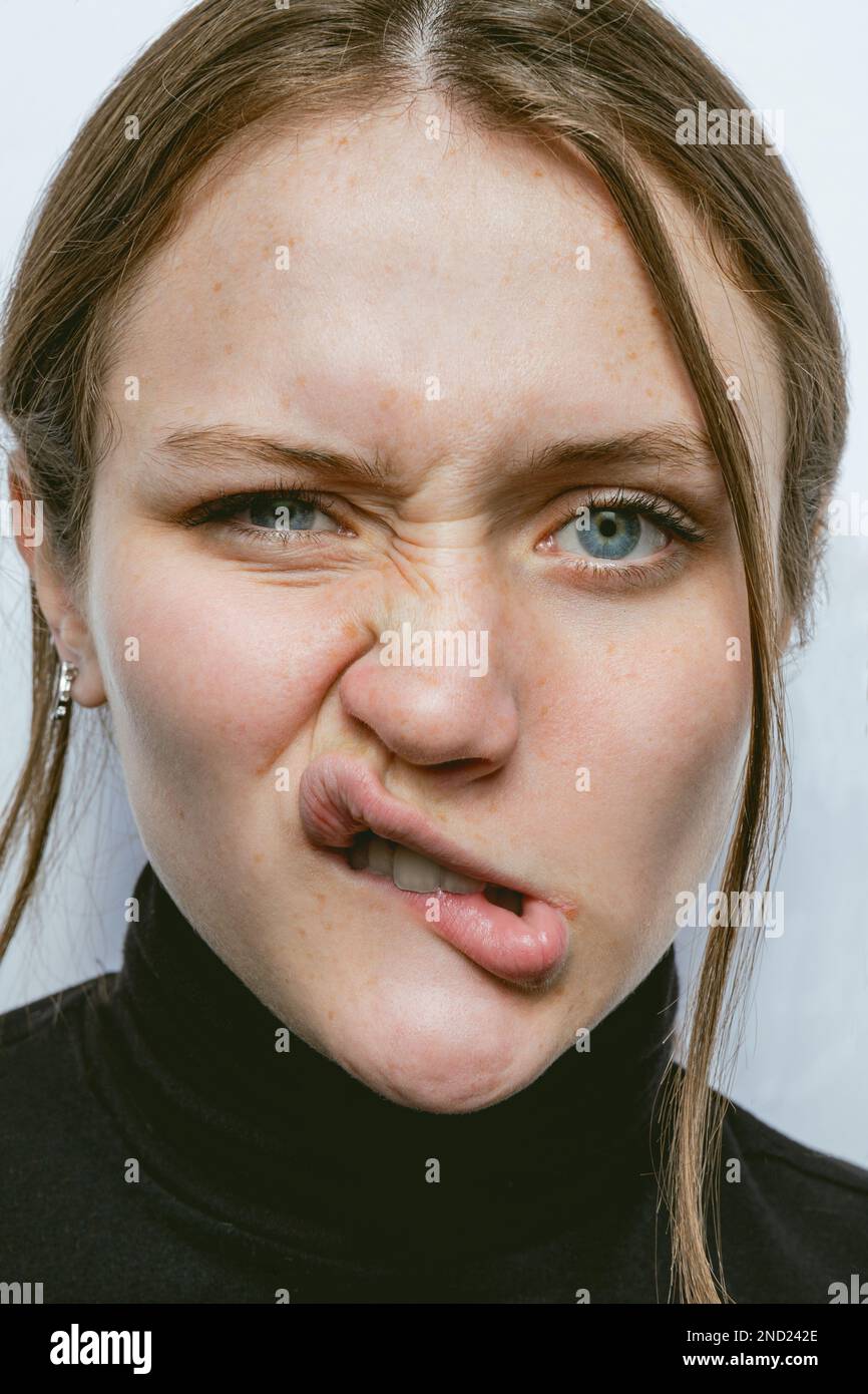 Porträt einer freudigen jungen Frau, die vor weißem Hintergrund Gesicht macht und in die Kamera schaut Stockfoto