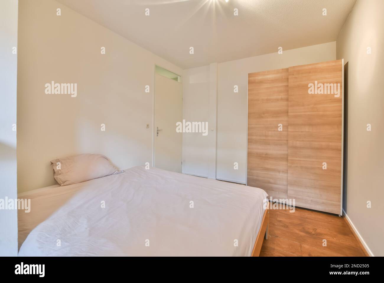 Innendesign des minimalistischen Schlafzimmers mit weißen Wänden, großem Bett und Holzparkett Stockfoto