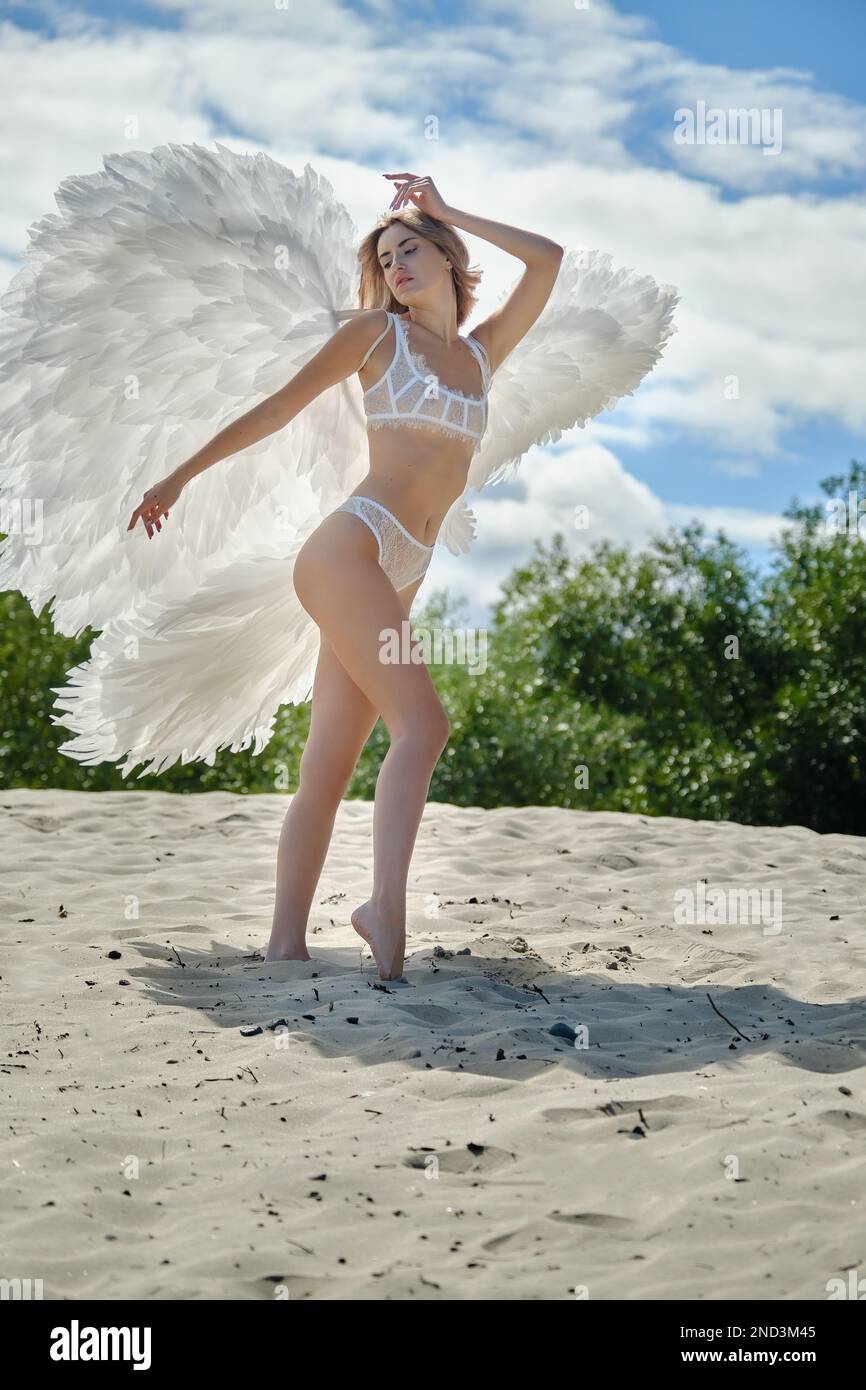 Ein junger, schöner weiblicher Engel mit weißen Flügeln auf Sand Stockfoto