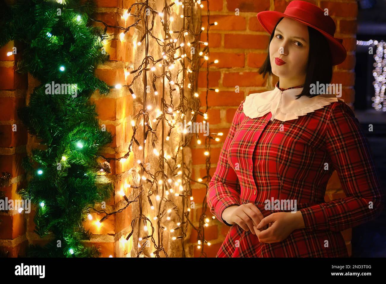 Neujahrsfeier, Feiertage, Weihnachten und Feierlichkeiten. Ein hübsches Mädchen in rotem Kleid, das draußen in der Nähe der Weihnachtsgirlande posiert Stockfoto