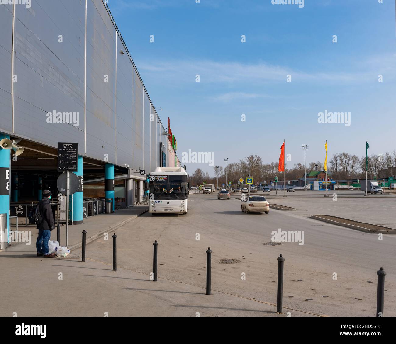 Nowosibirsk, Russland-12. April 2020. Ein einsamer Mann mit einer medizinischen Maske steht mit Einkaufstüten am Auchan Hypermarkt und wartet auf einen Bus wegen der Stockfoto