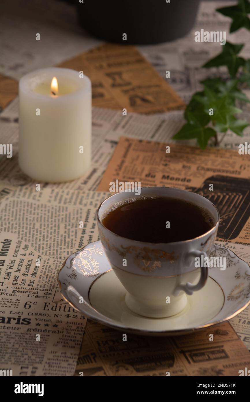Foto auf alten Zeitungsausschnitten, es gibt eine Tasse Kaffee neben einer brennenden Kerze Stockfoto
