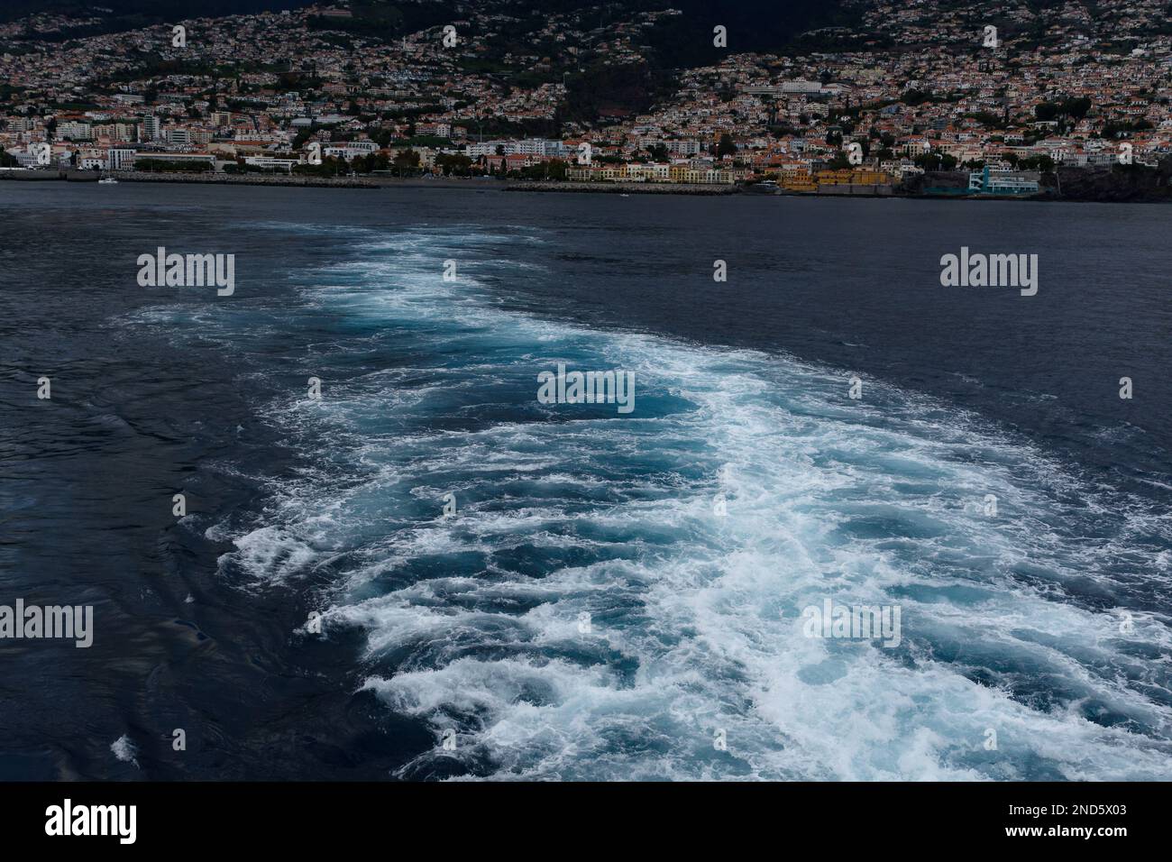 Kreuzfahrtschiff wird aktiviert, wenn das Schiff Funchal, Madeira, verlässt. Funchal ist im Hintergrund. Schönes weißes und blaues Wasser. Stockfoto