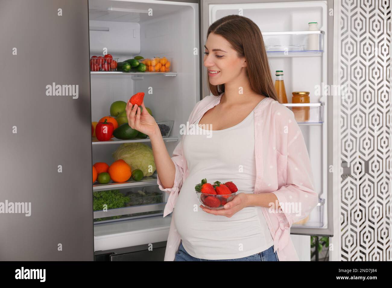 Junge schwangere Frau mit Erdbeeren in der Nähe des Kühlschranks zu Hause. Gesunde Ernährung Stockfoto