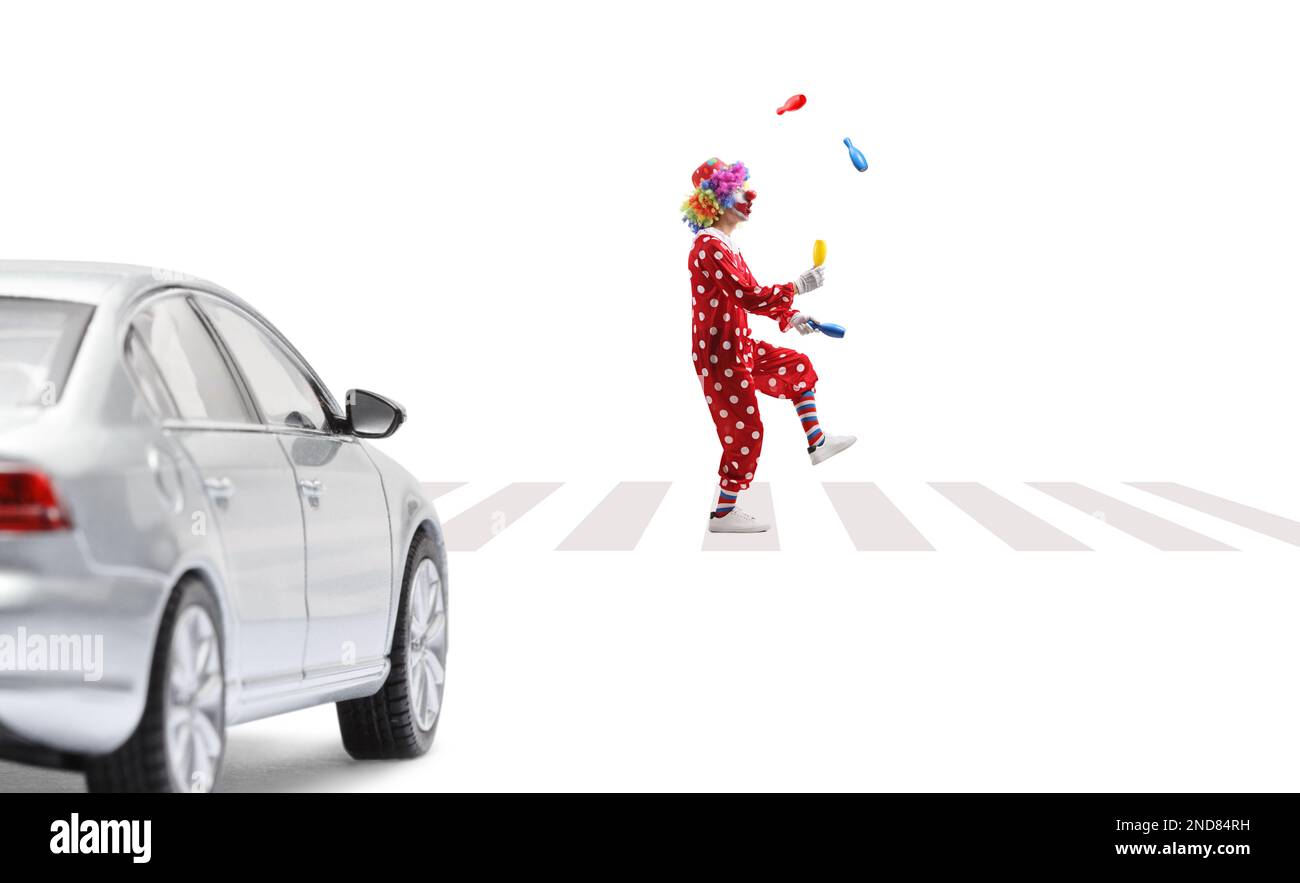 Ein Clown jongliert an einem Fußgängerübergang und ein Auto wartet isoliert auf weißem Hintergrund Stockfoto