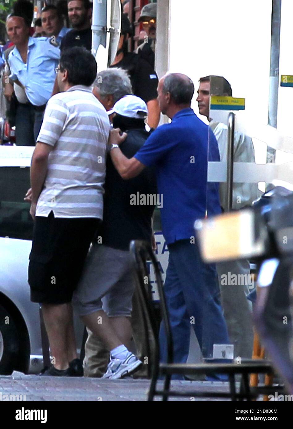 A bank robber, center with the white cap, surrounded by four hostages as Greek special police forces are seen in the background outside the National Bank of Greece, in the port of Piraeus, near Athens, Monday, Aug. 23, 2010. The man, armed with hand grenades and a gun, surrendered to police after holding several people in the bank hostage Monday following an attempted robbery, authorities said. (AP Photo/Thanassis Stavrakis) Stockfoto