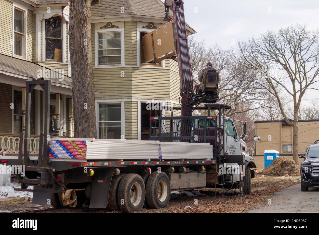 Arbeiter, die Kran benutzen, um Trockenbauwände durch das Fenster im zweiten Stock des historischen viktorianischen Hauses, Oak Park, Illinois, zu laden. Stockfoto