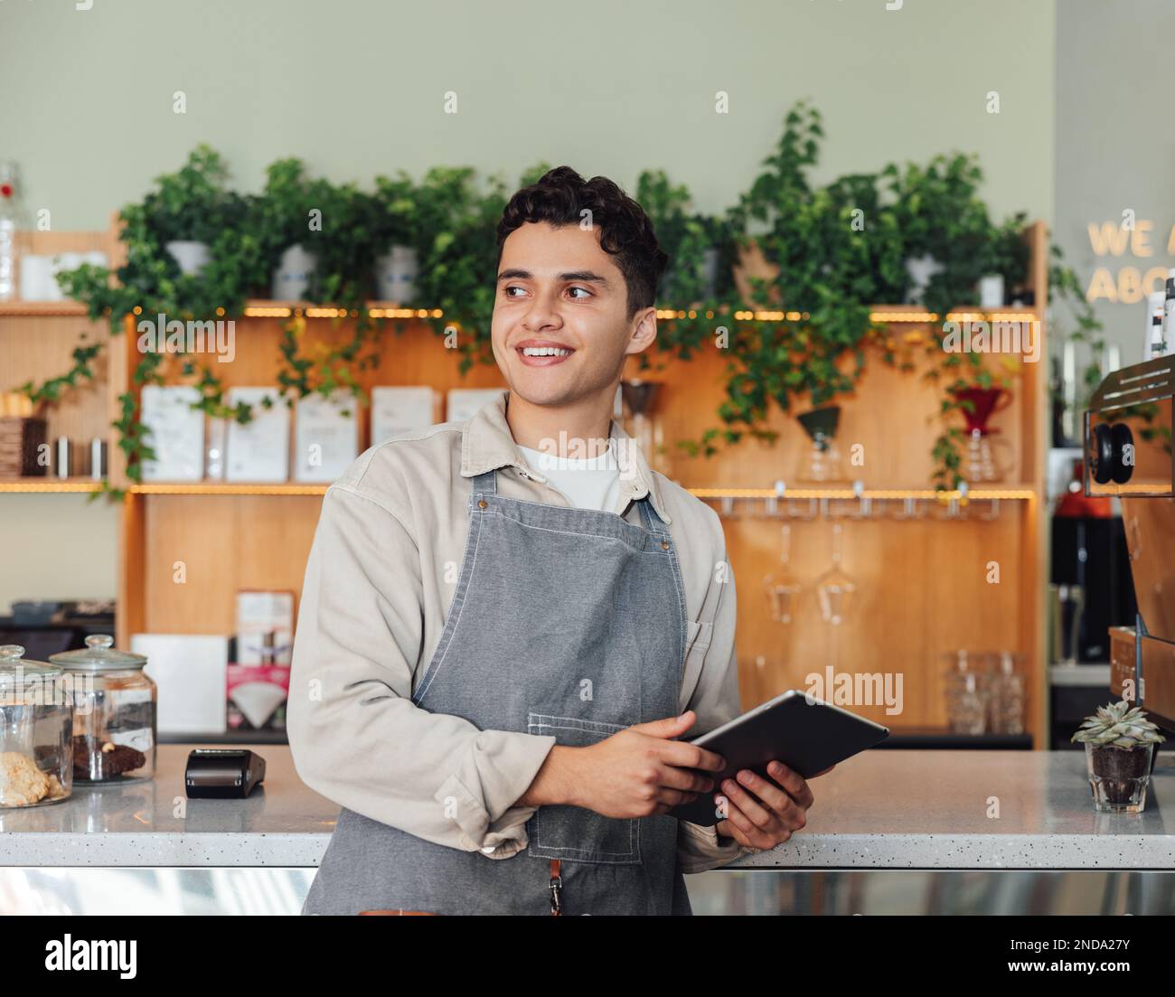 Männlicher Coffee-Shop-Besitzer in der Schürzentheke. Nahöstlicher Barista, der ein digitales Tablet hält und wegschaut. Stockfoto