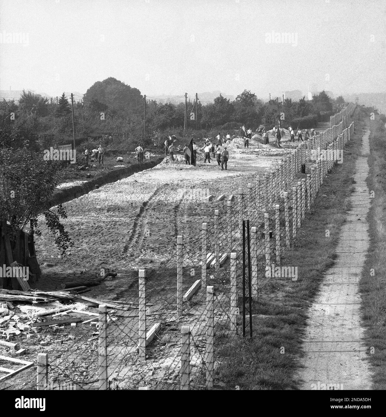 East Berlin laborers work on “Death Strip” which communist authorities created on their side of the border in the divided city on Oct. 1, 1961. A double barbed wire fence marks the border, with West Berlin at right. In this view of the area on September 23 laborers level rubble of houses which, just days before, stood on the site close to the border. Buildings along the 25-mile dividing line were evacuated and razed by Berlin reds to eliminate one means of escape used by East Berliners to jump to the west. (AP Photo/Eddie Worth) Stockfoto