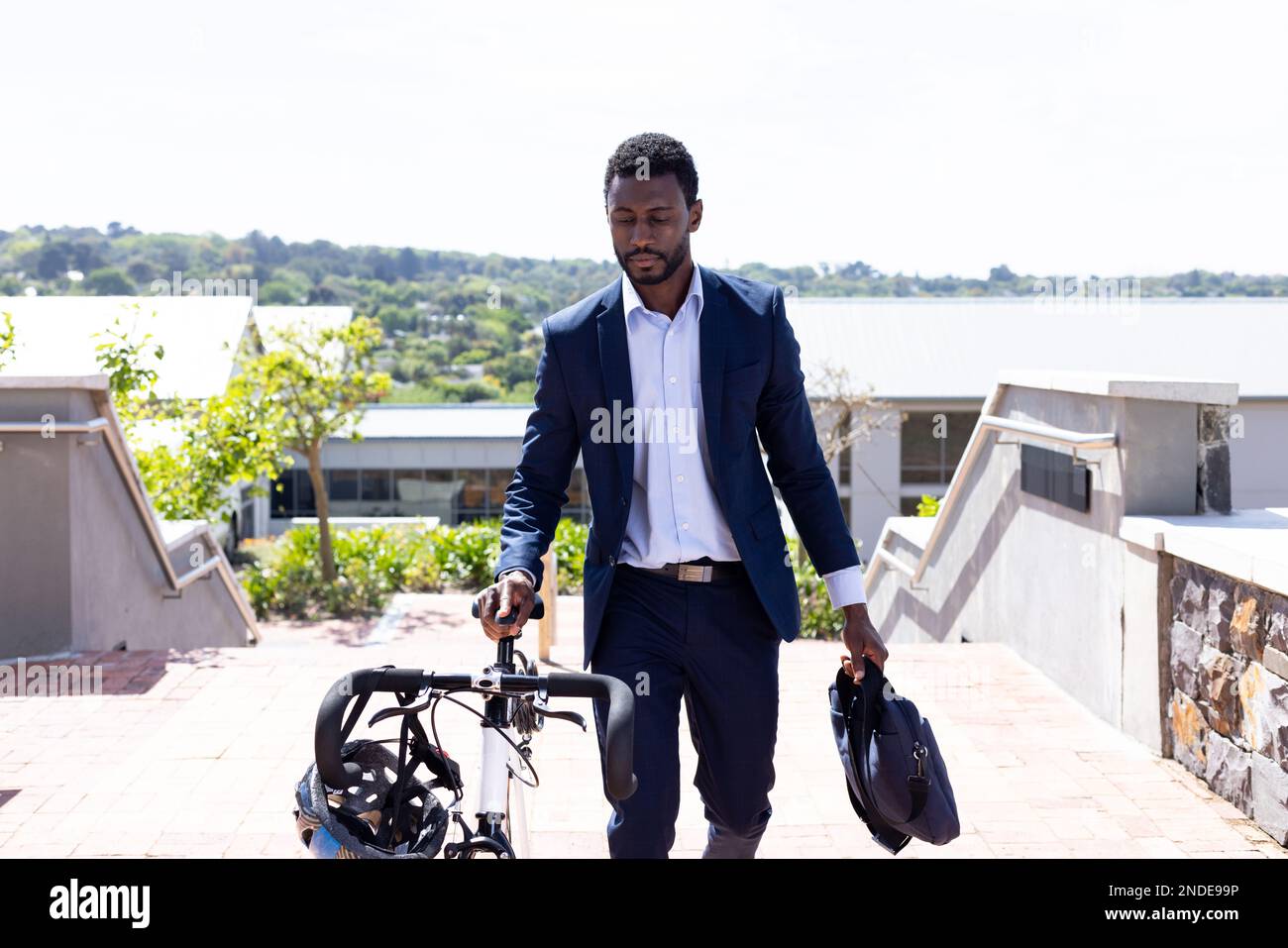 Ein afroamerikanischer Geschäftsmann, der Anzug trägt und mit dem Fahrrad zur Arbeit geht, mit einer Tasche Stockfoto