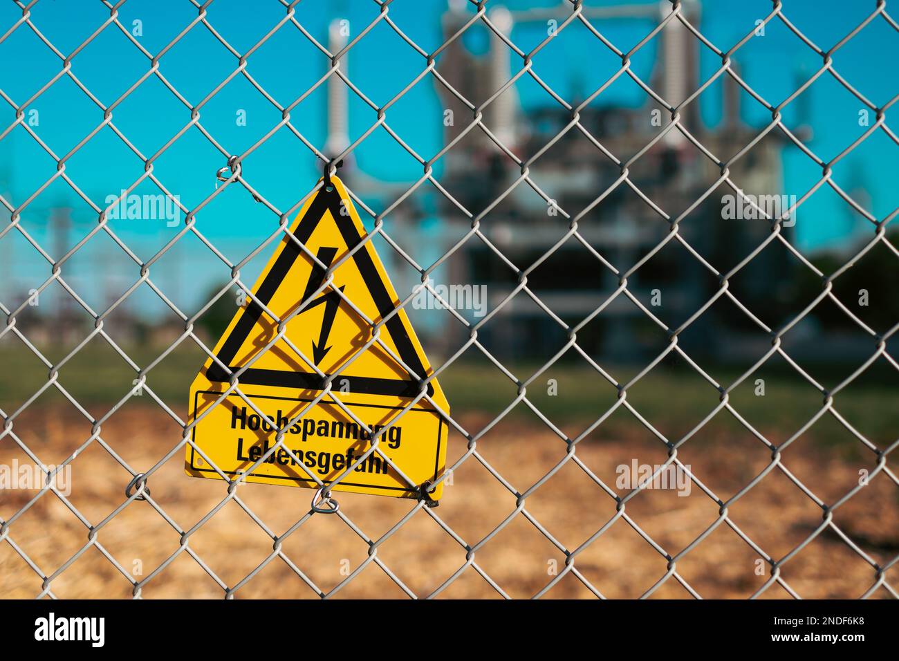 Gelbes Gefahrenzeichen Hochspannungsgefahr an Metallzaunen vor einer elektrischen Umspannstation in Deutschland Stockfoto