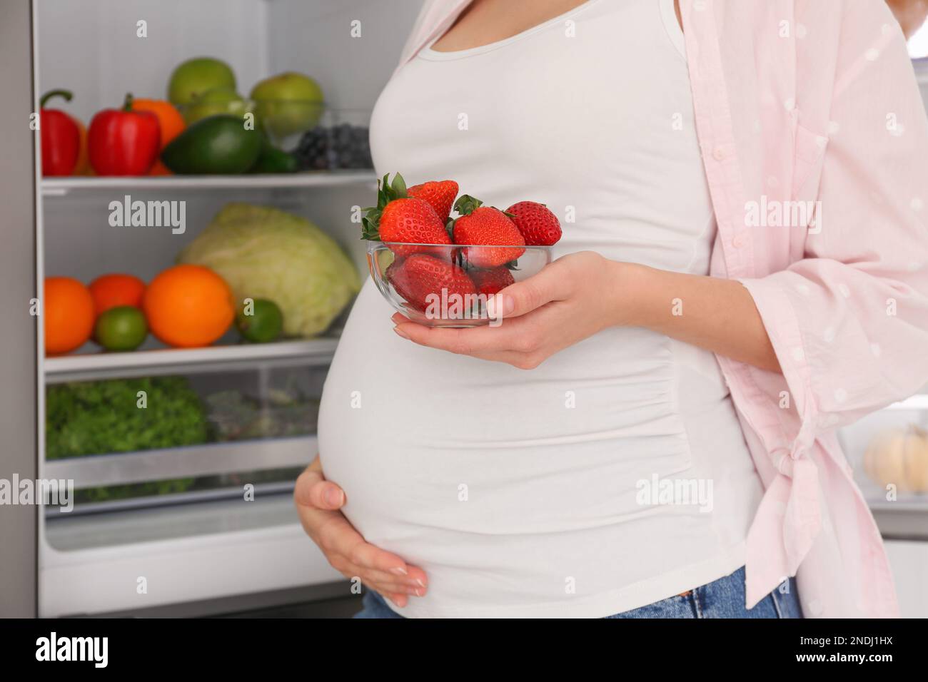 Junge schwangere Frau mit Erdbeeren in der Nähe des Kühlschranks zu Hause, Schließung. Gesunde Ernährung Stockfoto