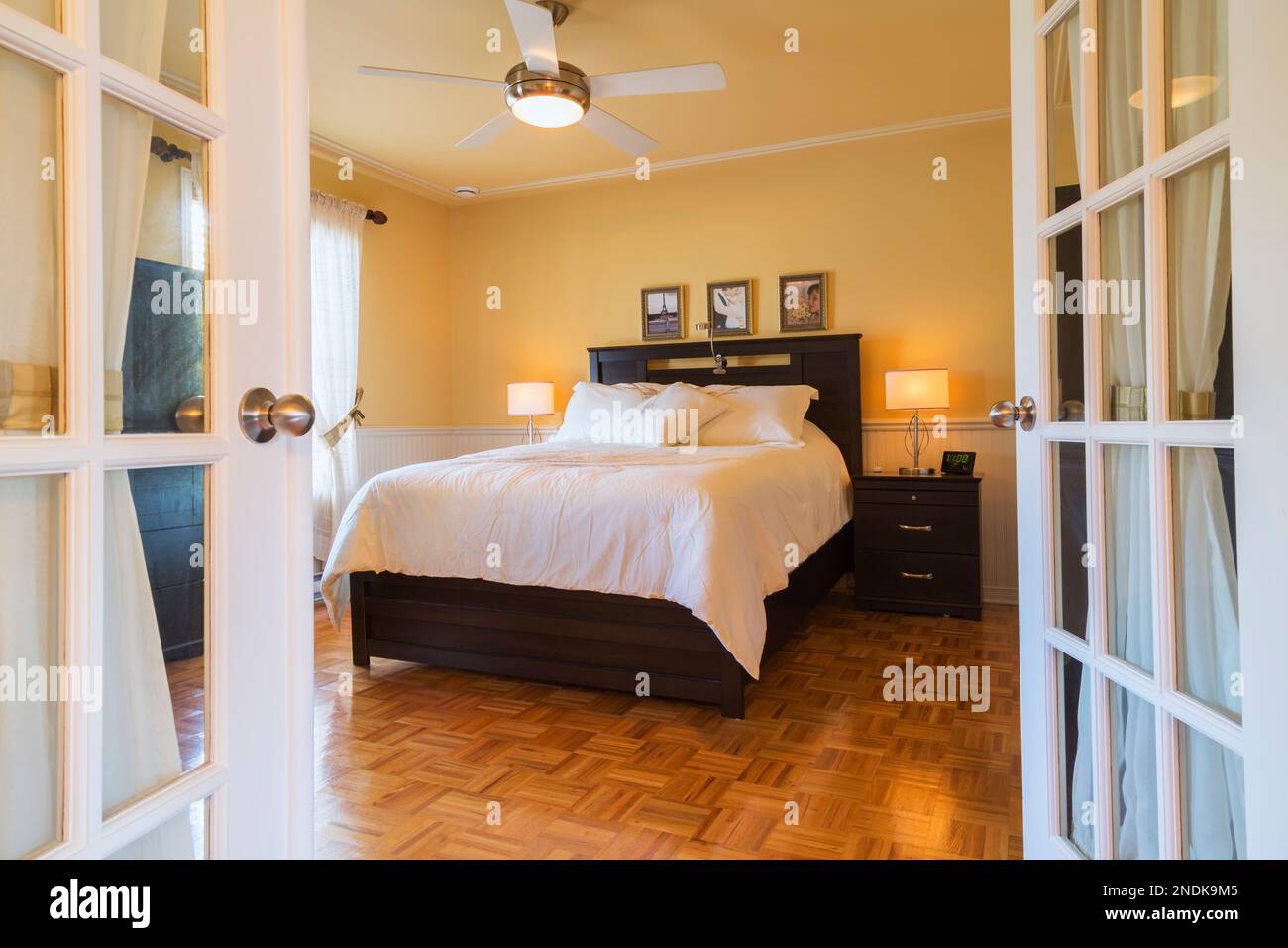 Queen-size-Bett mit Holz Kopfteil, Beistelltisch und offenen französischen Türen im oberen Hauptschlafzimmer im Landhausstil. Stockfoto