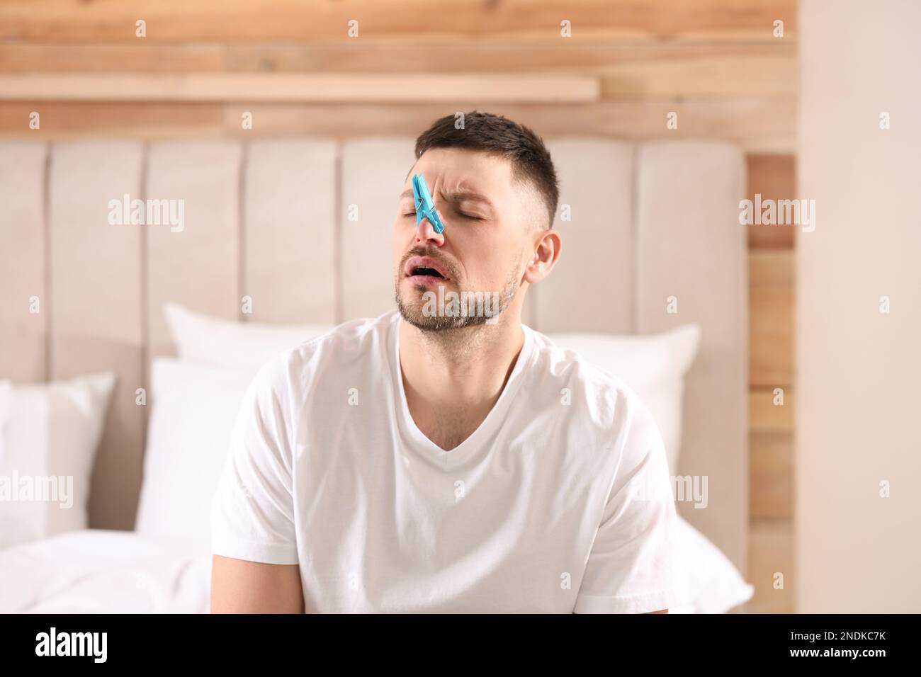 Ein Mann mit Wäscheklammer, der an einer laufenden Nase im Schlafzimmer leidet Stockfoto