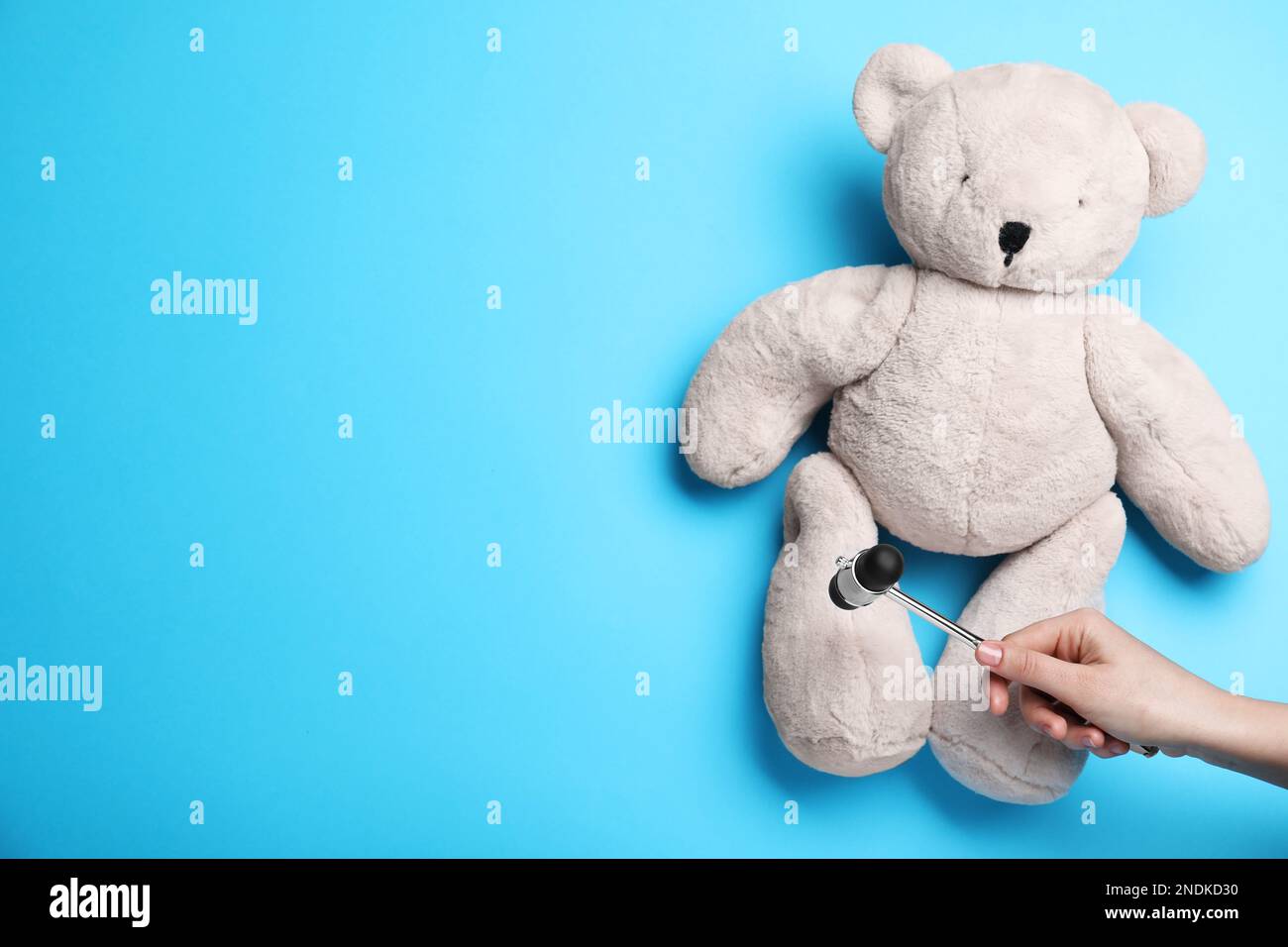 Frau, die vorgibt, die Reflexe des Teddybären mit einem Hammer auf hellblauem Hintergrund zu testen, Nahaufnahme und Platz für Text. Diagnostik des Nervensystems Stockfoto