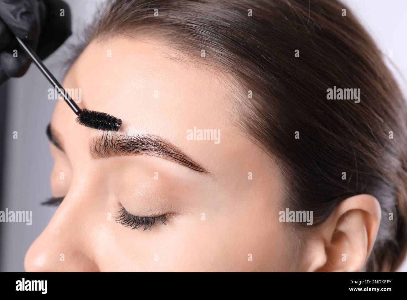 Kosmetikerin putzt die Augenbrauen von Frauen, nachdem sie auf hellem Hintergrund getönt hat, Nahaufnahme Stockfoto
