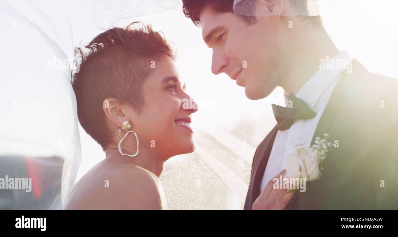 Es ist einfach ein glücklicher Moment. Ein liebevolles junges Ehepaar, das einen intimen Moment teilt, während es sich mit einem Schleier auf seiner Hochzeit bedeckt Stockfoto