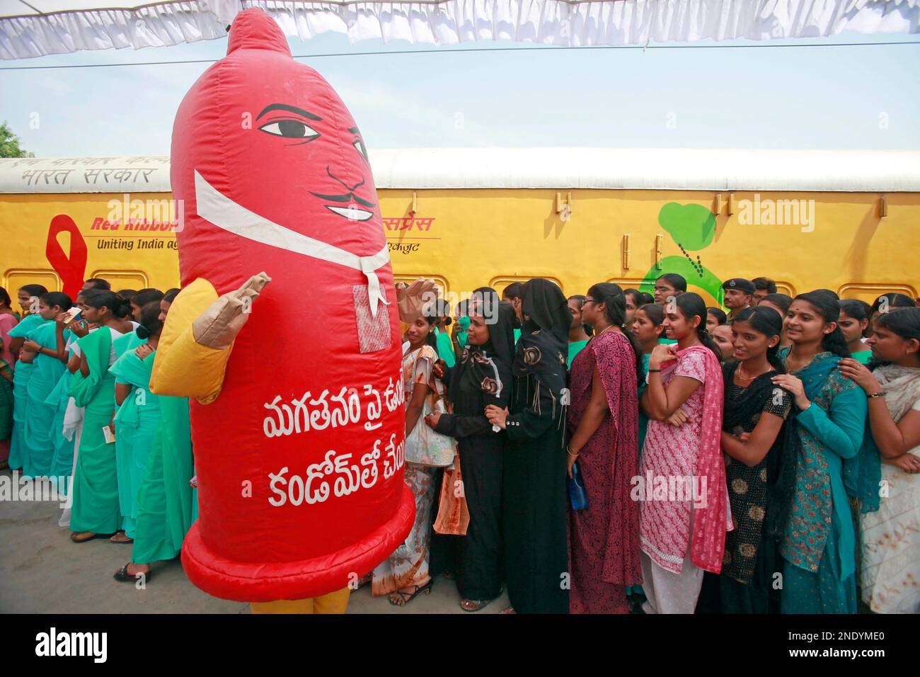 Red Ribbon Express A person dressed as a giant condom walks past visitors standing in a ...
