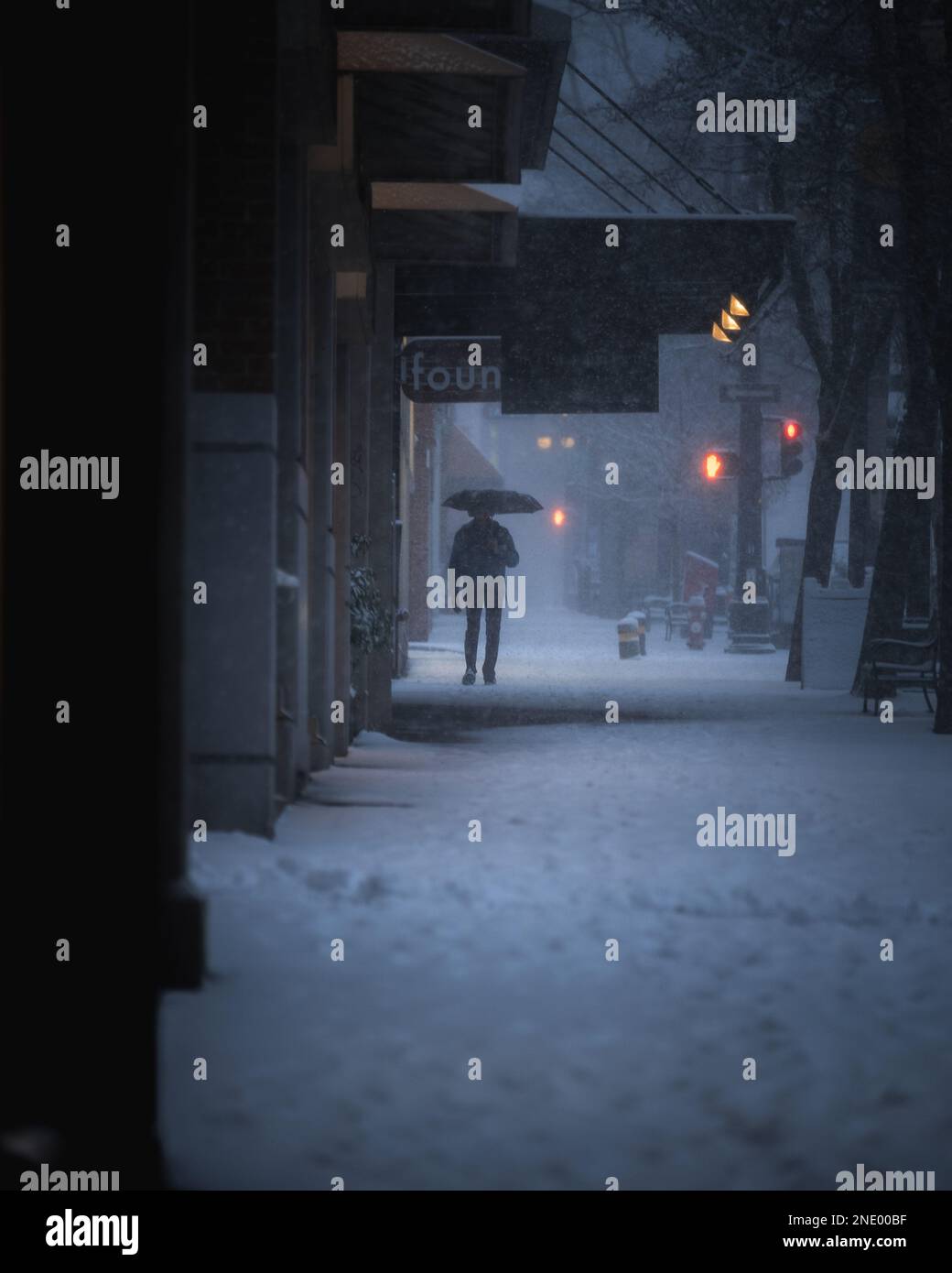Mann mit Schirm, der während eines Schneesturms auf der Straße spaziert Stockfoto