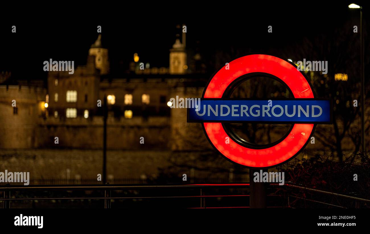 Das beleuchtete Schild der Londoner U-Bahn vor dem Londoner Turm, königliches Gebäude bei Nacht Stockfoto