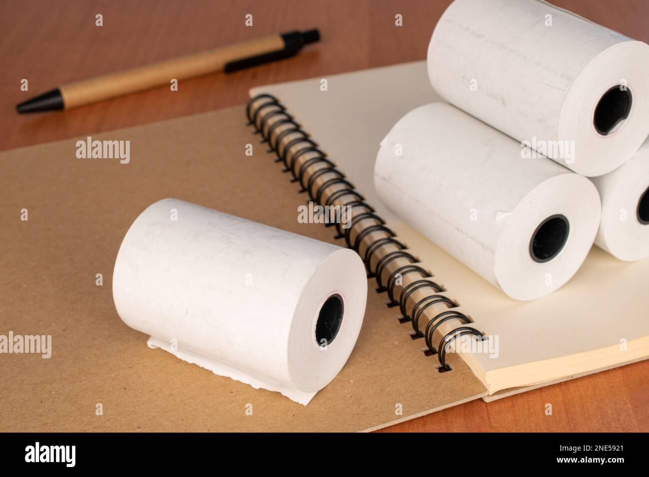 Mehrere Papierrollen Kassenband mit Notizbuch und Stift auf dem Schreibtisch, Nahaufnahme. Stockfoto