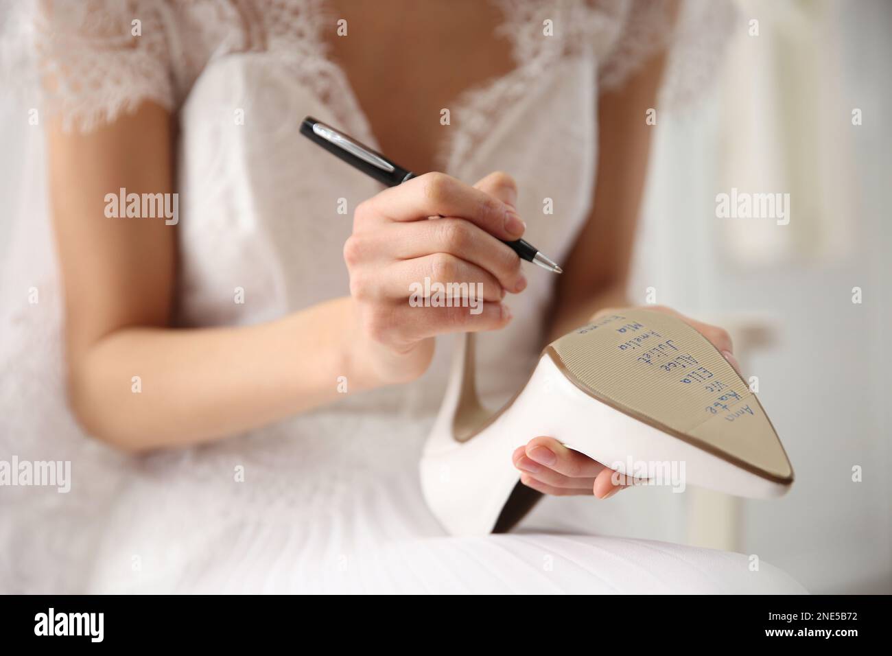 Die junge Braut schreibt die Namen ihrer Single-Freunde drinnen auf Schuhe, Nahaufnahme. Hochzeitsabergläubisch Stockfoto