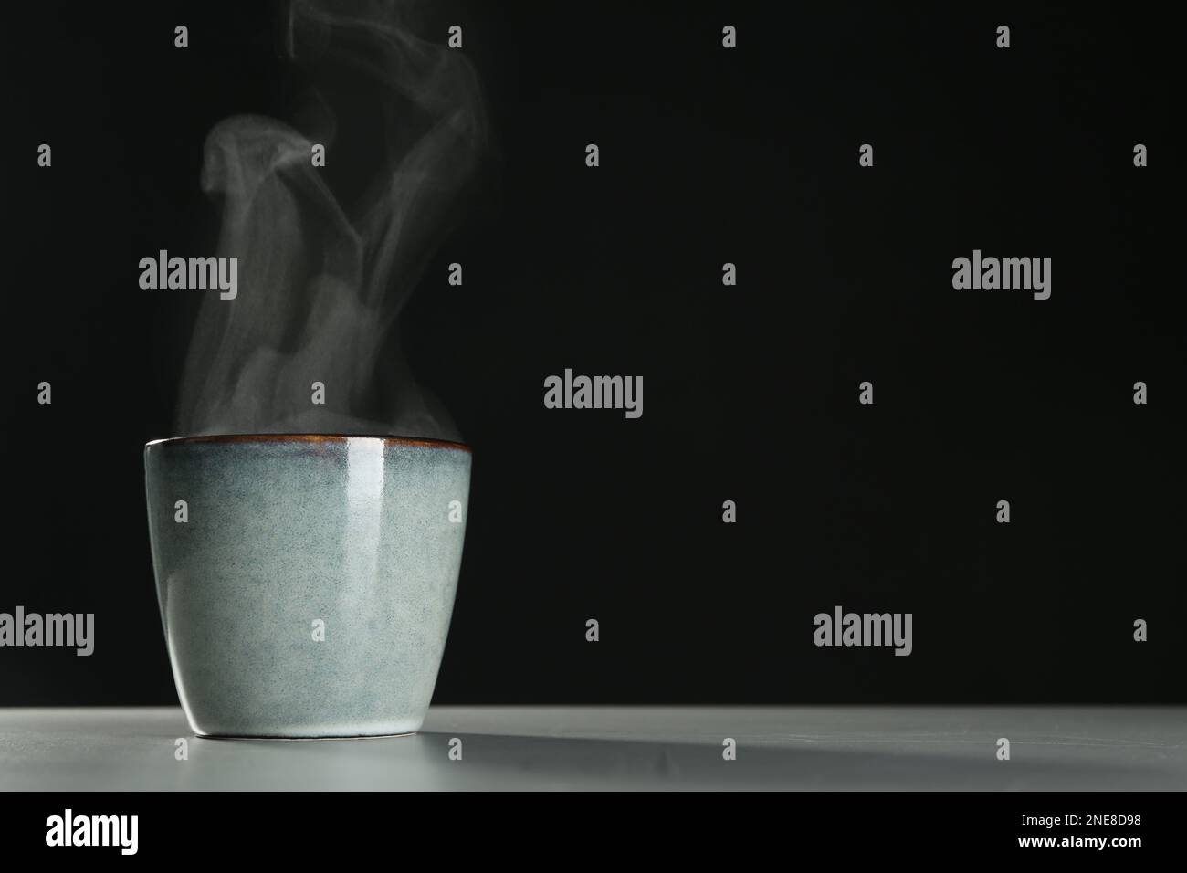 Tasse mit Dampf auf dem Tisch vor schwarzem Hintergrund. Platz für Text Stockfoto