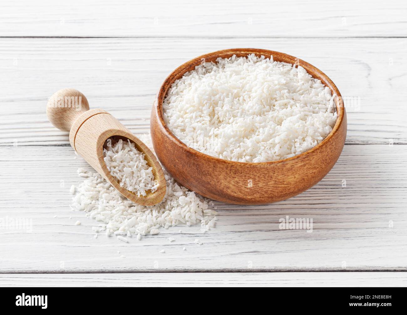 Kokosflocken in Holzschüssel mit Schaufel auf weißem Holzhintergrund Stockfoto