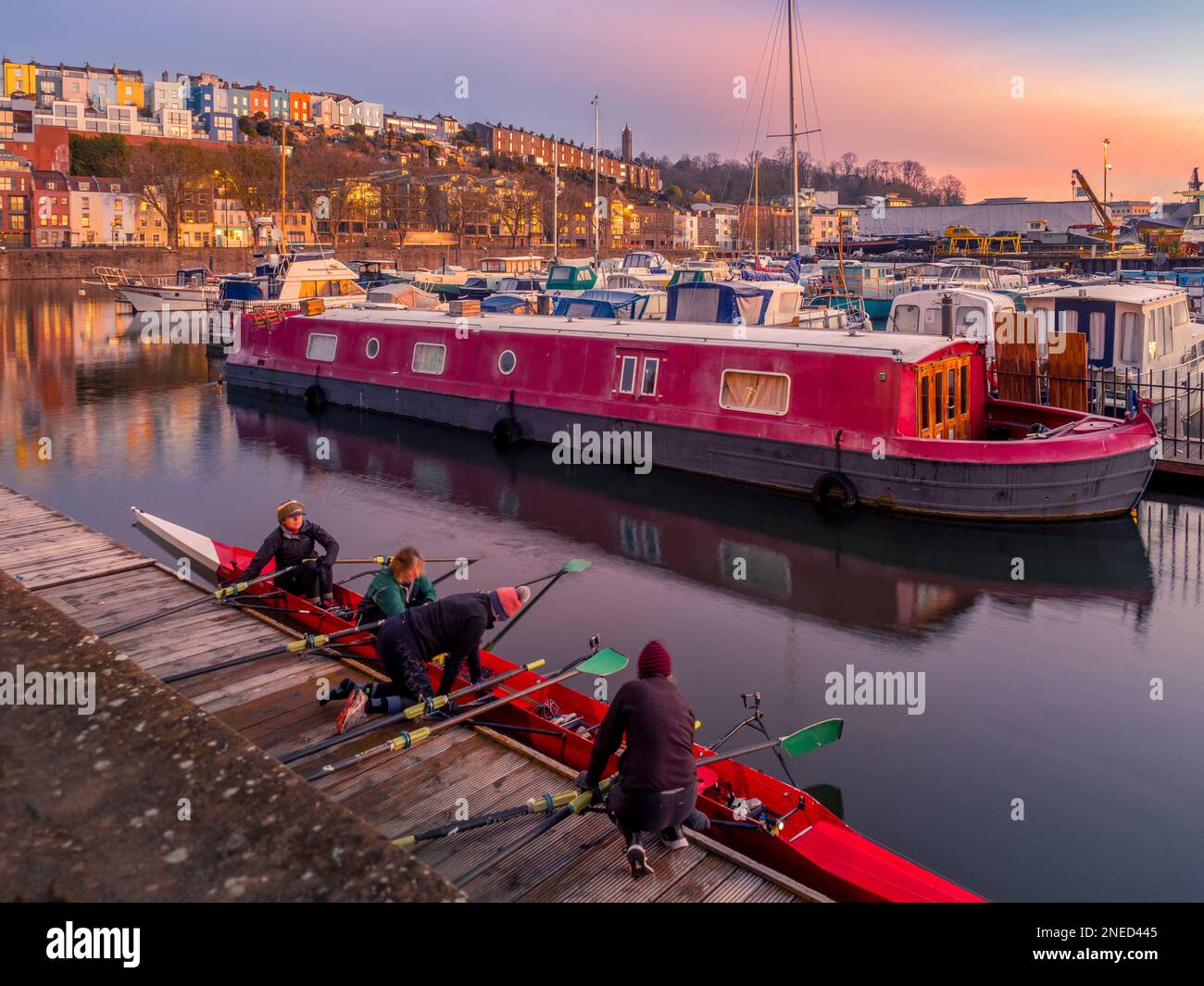 Ruder bereiten ihr Boot bei Sonnenaufgang in Bristol Marina vor, mit den farbenfrohen Terrassenhäusern von Cliftonwood in der Ferne. Bristol. UK. Stockfoto