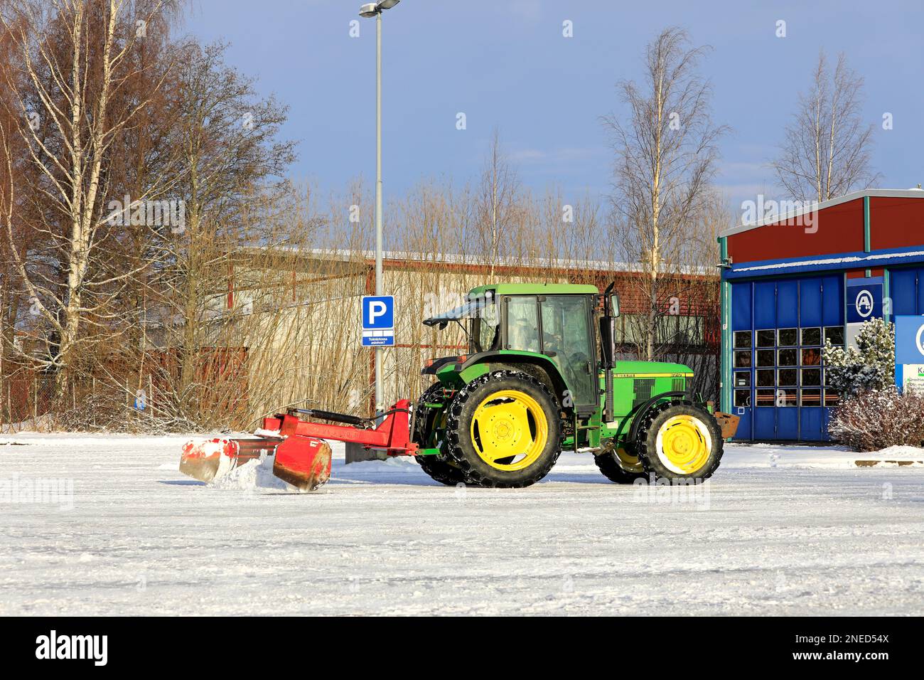 Schneeräumung vom Parkplatz mit John Deere 6010-Traktor und Heckmesser nach Schneefall im Winter. Salo, Finnland. 11. Februar 2023. Stockfoto