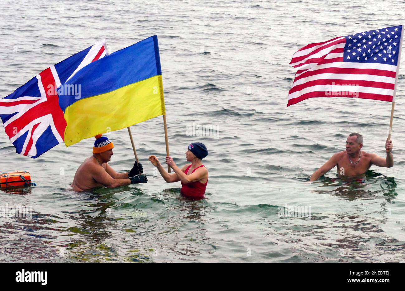 ODESA, UKRAINE - 16. FEBRUAR 2023 - Lokale Winterschwimmer halten die Flaggen von Großbritannien, der Ukraine und den USA während der Feier des Tages der Einheit, Odesa, so Stockfoto