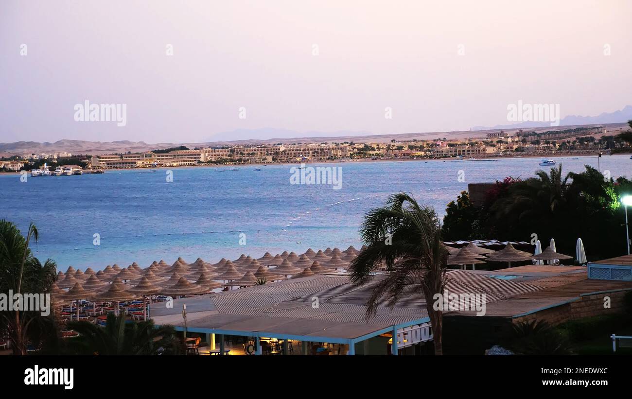 Ägyptisches Resort. Eine von vielen ruhigen Buchten des Roten Meeres, bei Sonnenuntergang, in der Dämmerung. Vor dem Hintergrund der Umrisse von Gebäuden, Palmen, Bergen. Hochwertiges Foto Stockfoto